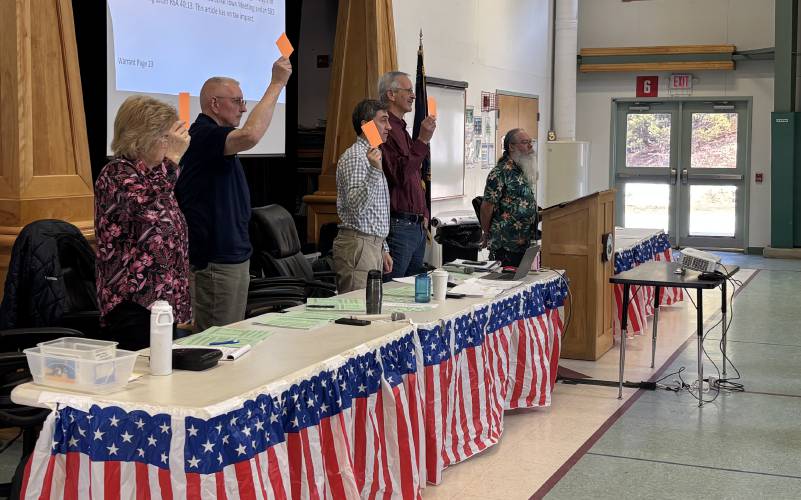From left, Town Clerk Dorene Adams and Select Board members Mike Borden, Mason Parker and Tom Bascom show their cards in a vote as Moderator Andres Wood looks on. 